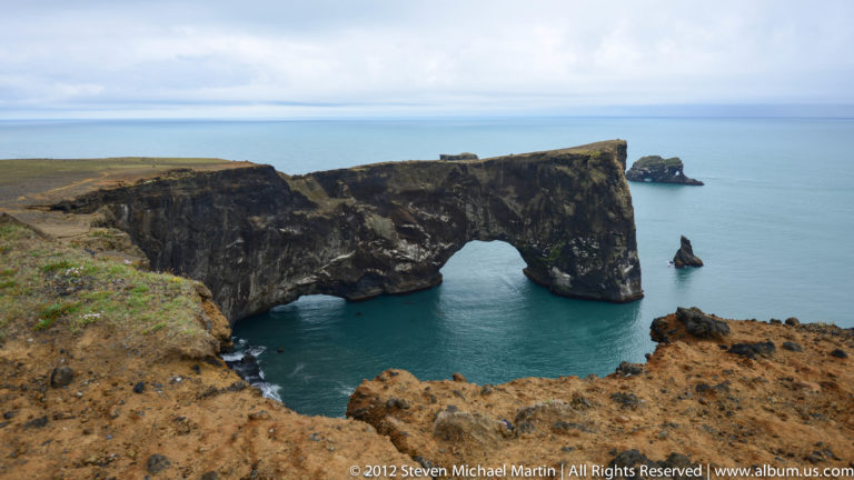 Dyrhólaey basalt headland with its large natural sea arch, a smaller opening, and an offshore stack.