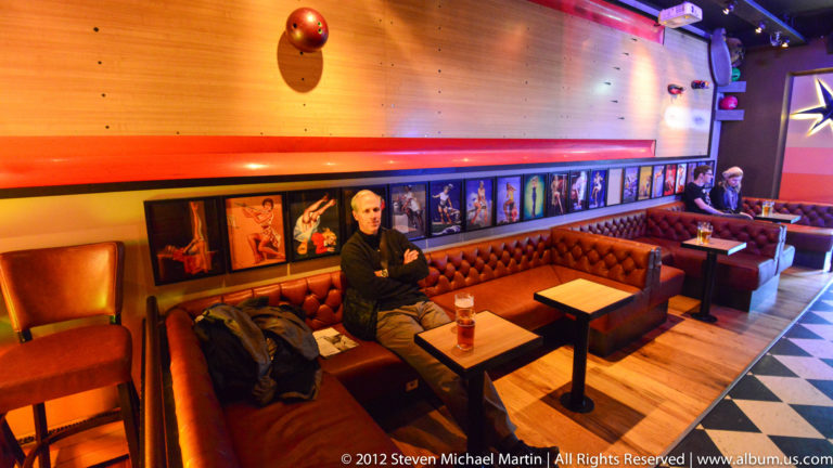 A man sits in an orange booth beneath colorful wall displays and vivid red and purple lighting.