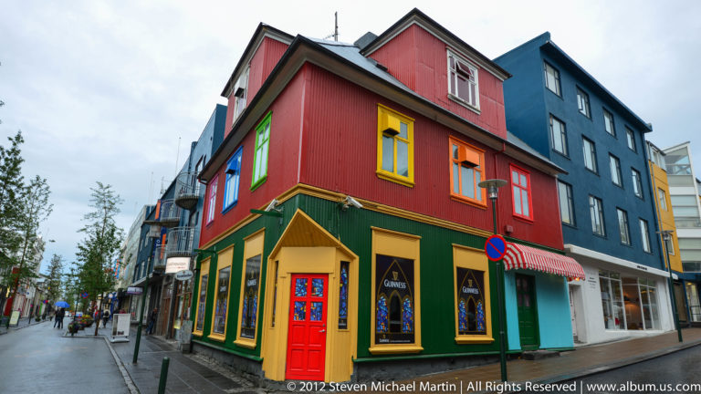 Colorful Reykjavík shop façades line a sidewalk, with a black Guinness sign above the storefront.