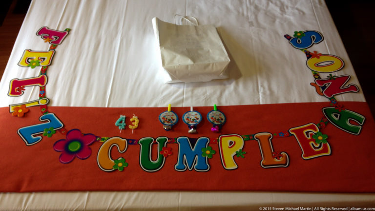 Colorful “Feliz Cumple” letters and small party decorations arranged across a red bed runner.