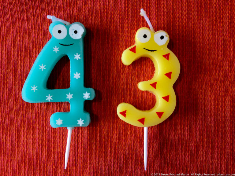 Turquoise number four and yellow number three birthday candles on red fabric.
