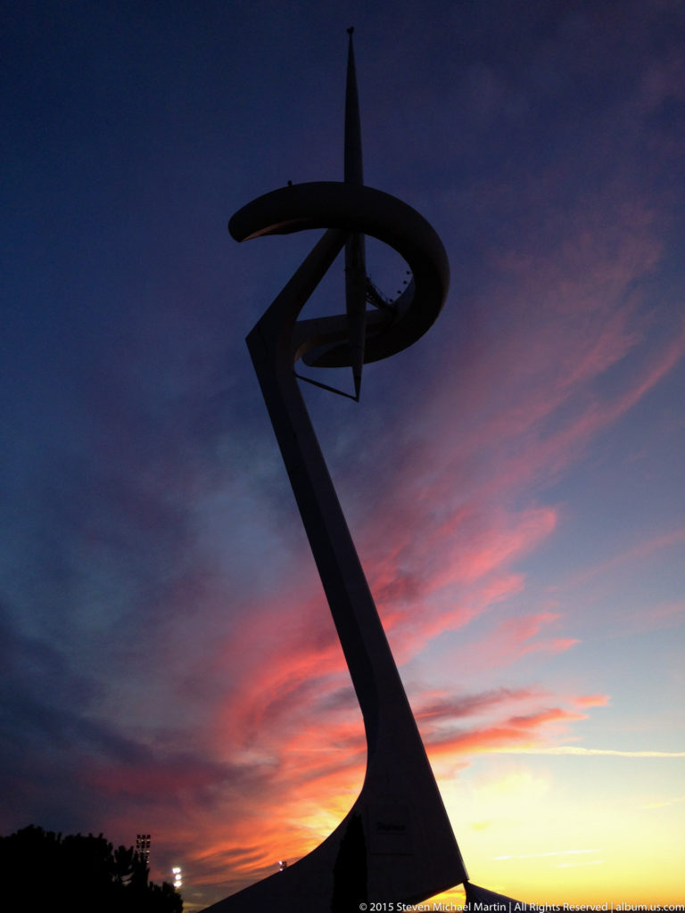 Silhouette of the Montjuïc Communications Tower against an orange and violet sunset.