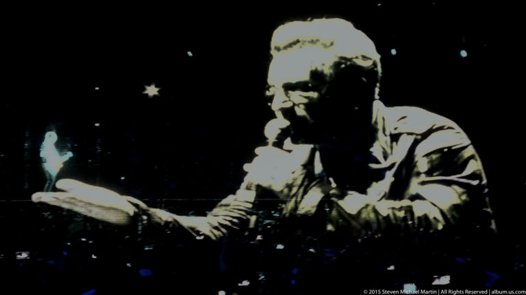 High-contrast black-and-white projection of a male performer extending one hand.