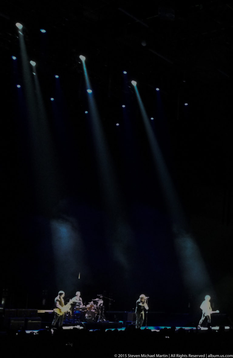 Small band members perform across a dark stage under several narrow spotlights.