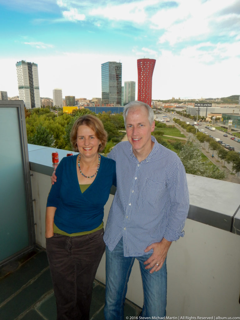 Woman and man pose together on a terrace with modern Barcelona towers in the background.
