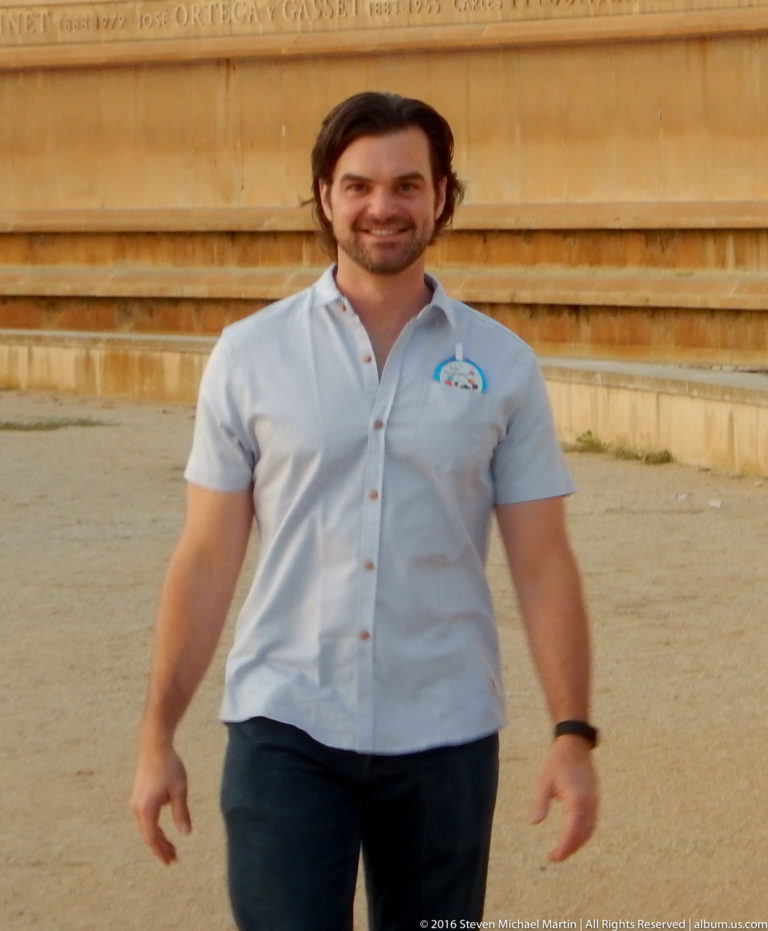 Smiling man in a light shirt standing before broad pale stone steps on Montjuïc.