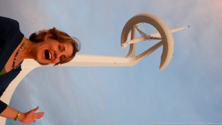 Woman leaning into the frame beneath the white Montjuïc Communications Tower at dusk.