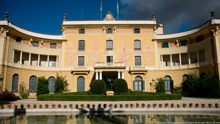 Symmetrical pale palace façade behind a formal garden and reflecting pool at Pedralbes.