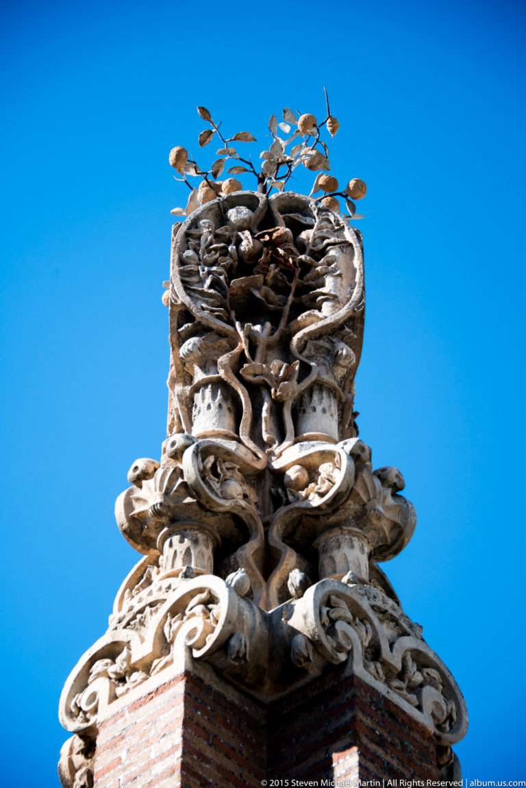 Highly sculpted rooftop finial with twisting organic ornament against a blue sky.