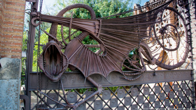 Large wrought-iron dragon with spread wings and open mouth across an entrance gate.