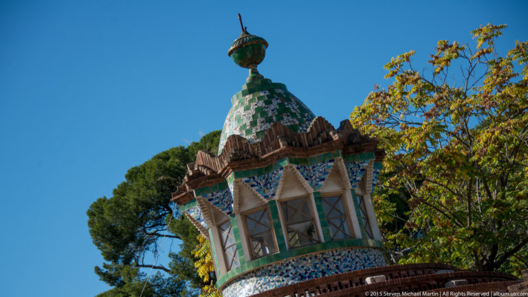 Low-angle view of a green-and-white mosaic roof lantern above brickwork and trees.