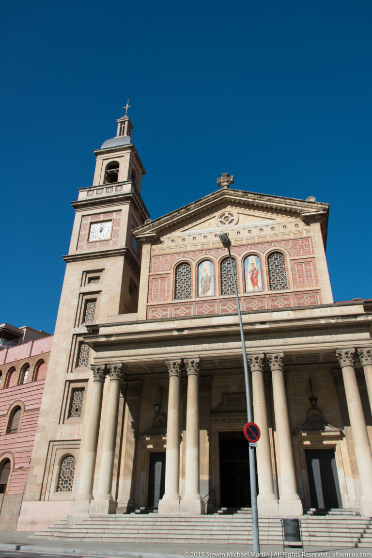 Church façade with broad columned portico, decorative panels, and square bell tower.