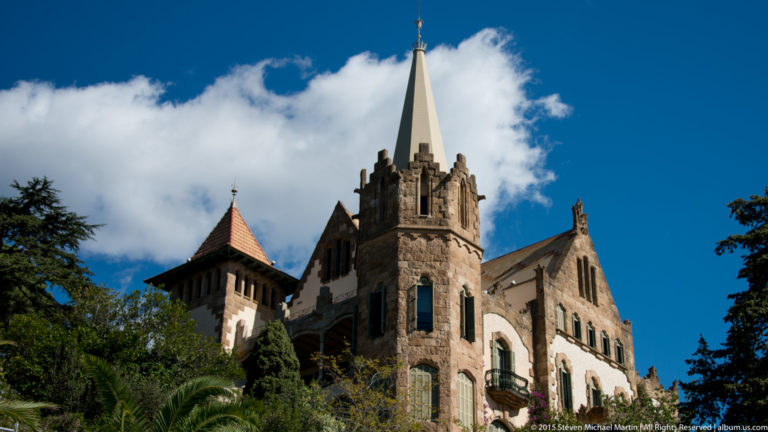 Stone Bellesguard house with Gothic forms, steep roofs, and a slender cross-topped spire.