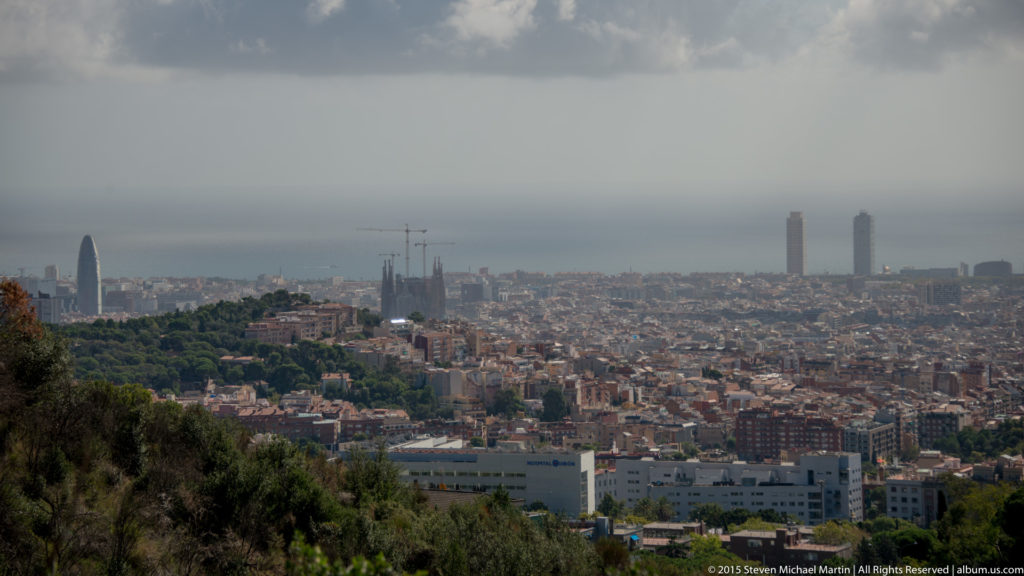 Hazy elevated panorama of Barcelona with Torre Glòries and distant waterfront towers.