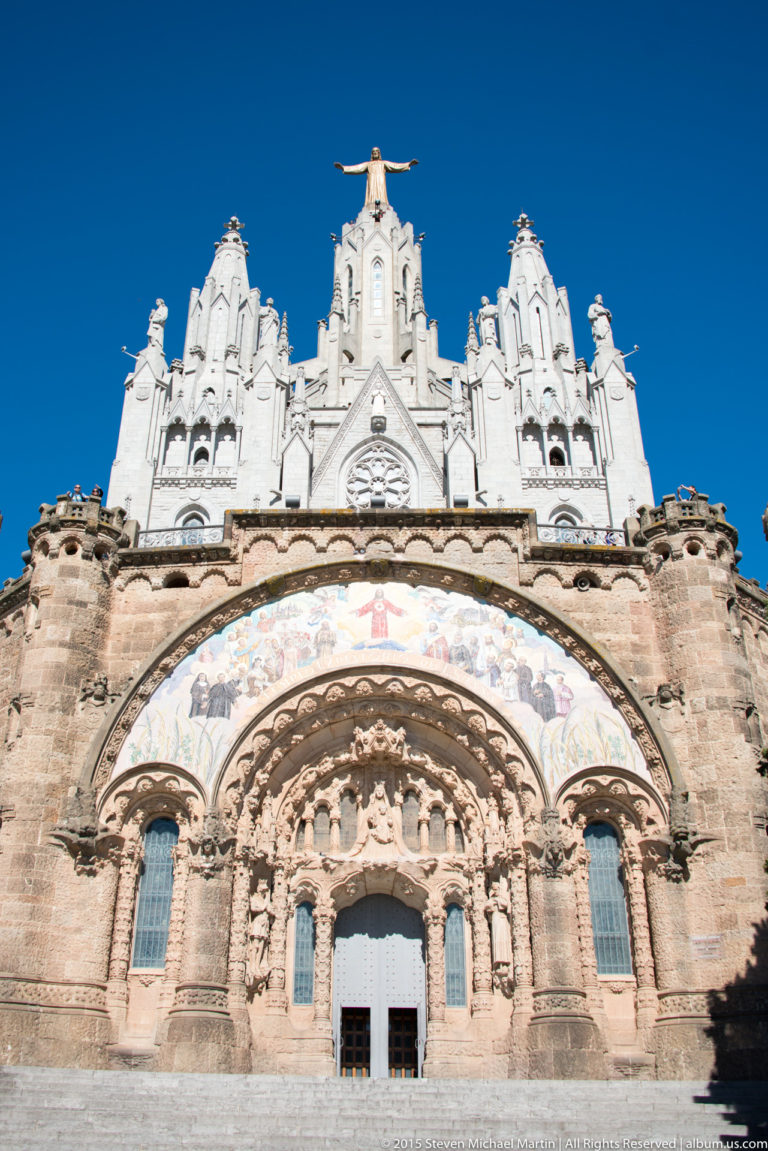 Stone portal with sculpted arches and mosaic beneath the white upper church of the Temple Expiatori del Sagrat Cor.