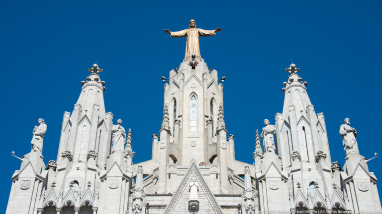 White Neo-Gothic towers of the Temple Expiatori del Sagrat Cor topped by a statue of Christ.