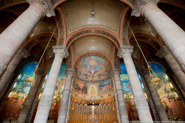 Church interior with pale columns, stained glass, and a richly colored mosaic apse.