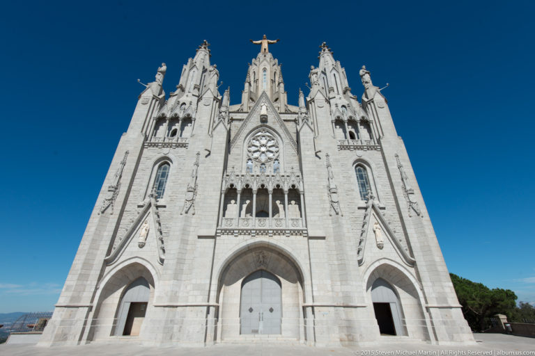Frontal white Neo-Gothic façade with pointed portals, rose window, pinnacles, and summit statue.