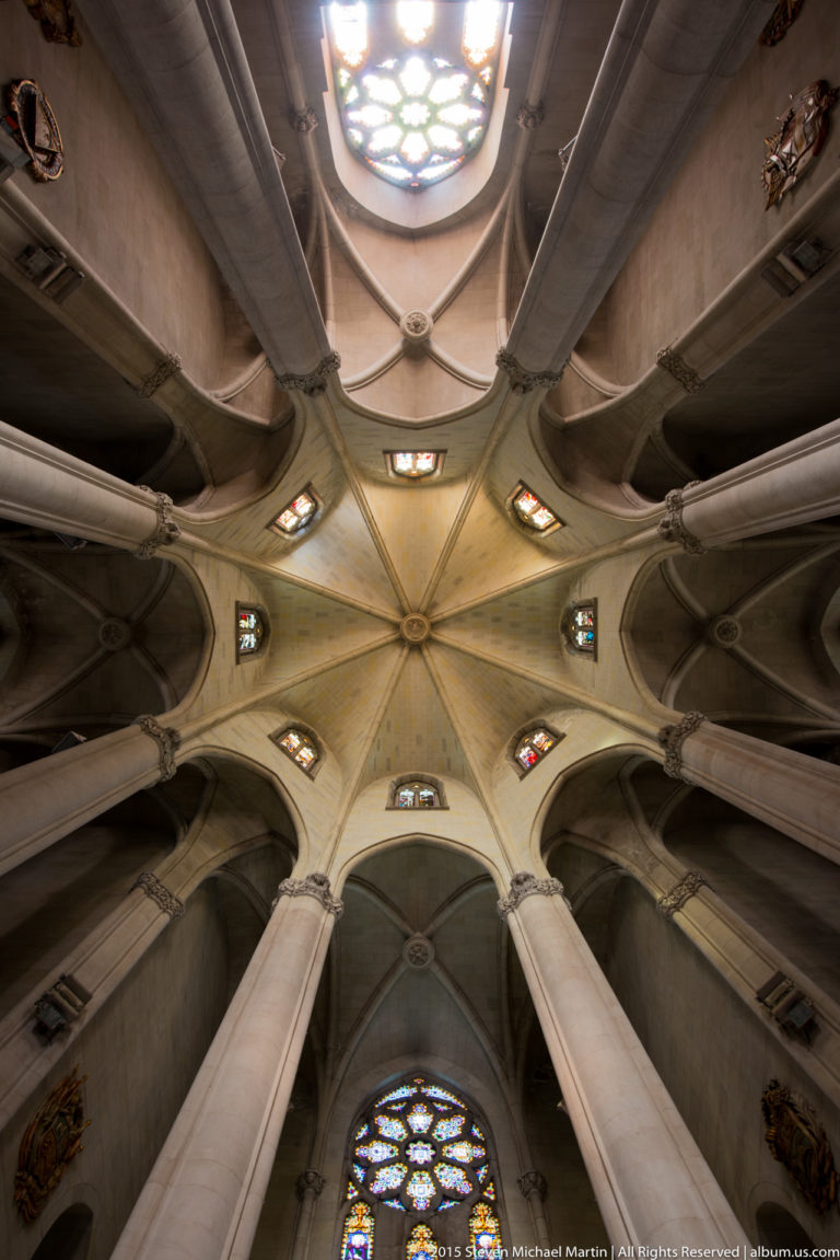 Upward view of ribbed vaults, columns, and stained-glass windows inside the Tibidabo church.