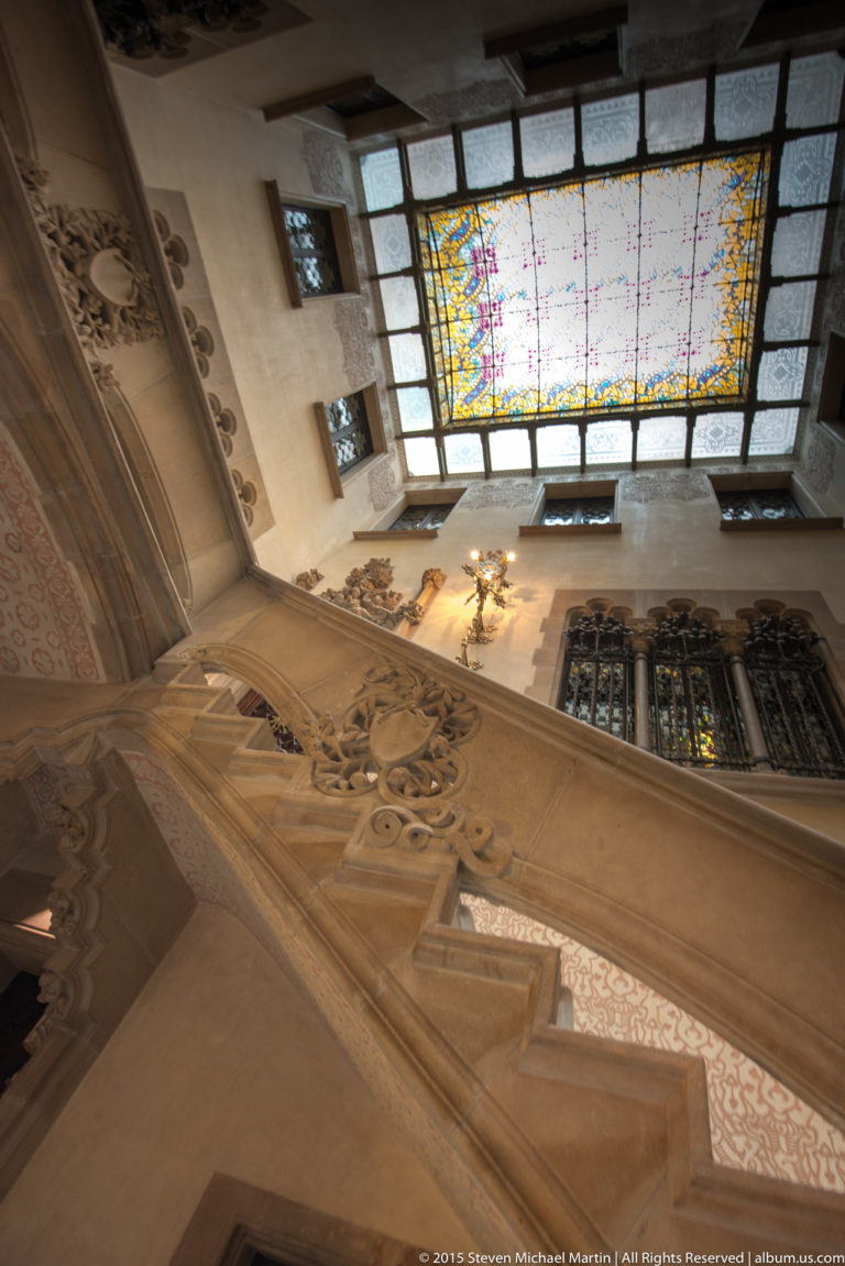 Ornate stone stair and decorative interior beneath a rectangular stained-glass skylight.