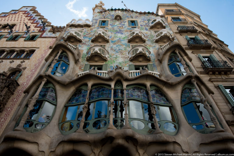 Low-angle view of Casa Batlló with curved stonework, irregular balconies, and blue-green mosaic.