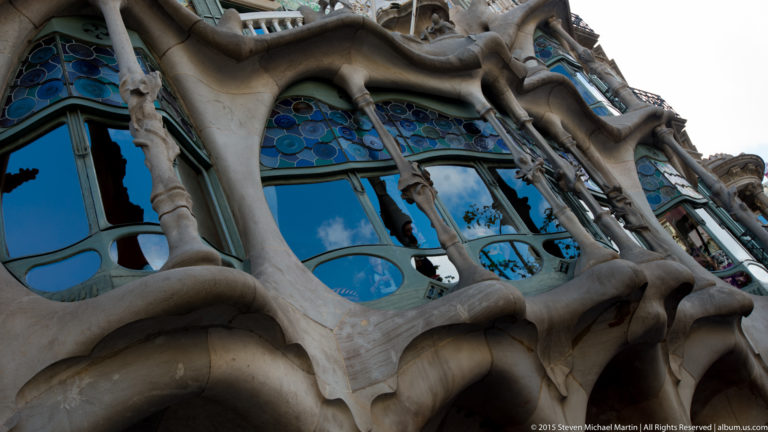 Curving bone-like stone columns frame blue glass windows on the lower façade of Casa Batlló.