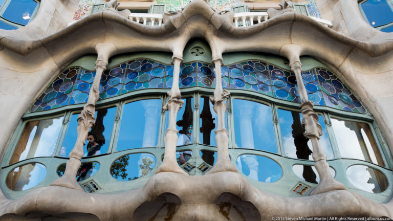 Casa Batlló window bay with branching stone mullions and blue-purple stained glass above.