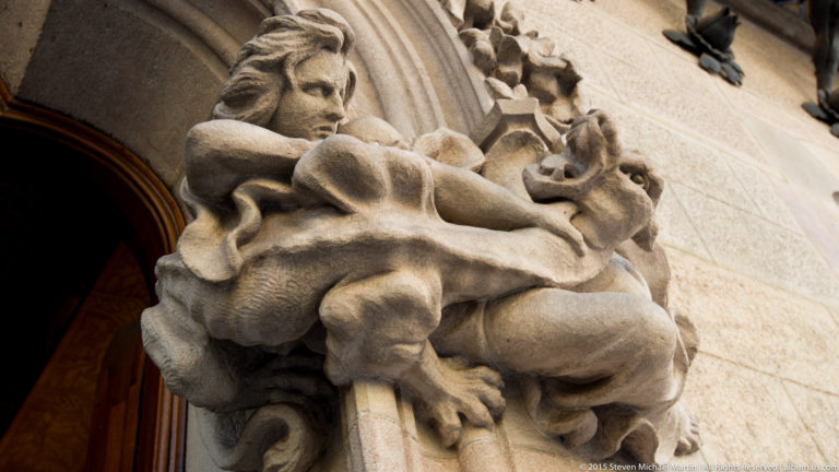 Carved stone figure with flowing drapery integrated beside an arched doorway.