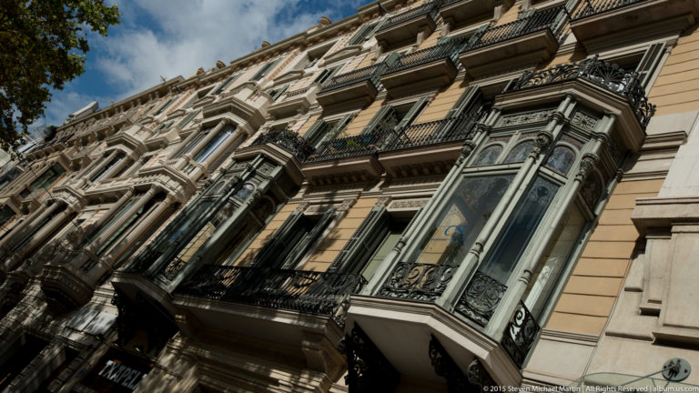 Upward street view of ornate Barcelona apartment façades with bay windows and wrought-iron balconies.