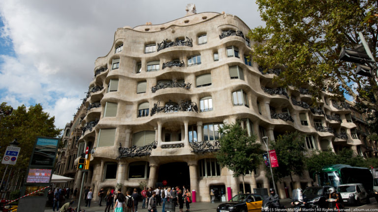 Casa Milà corner façade with undulating pale stone walls and dark wrought-iron balconies.