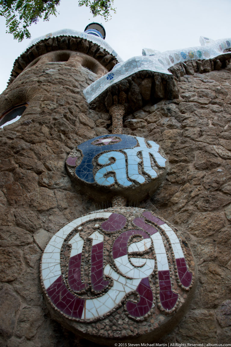 Round mosaic medallions spelling “Park Güell” mounted on a rough stone entrance wall.