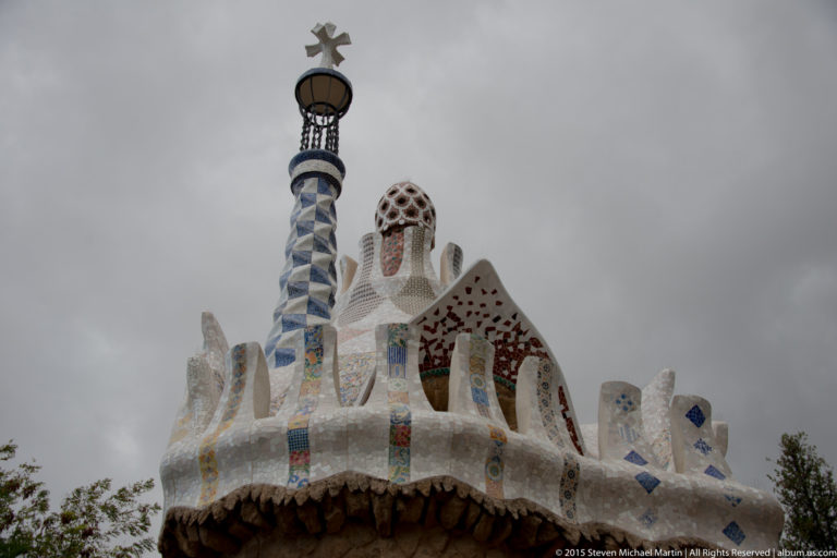 White mosaic roofline with colorful tile details and blue-and-white tower at Park Güell.