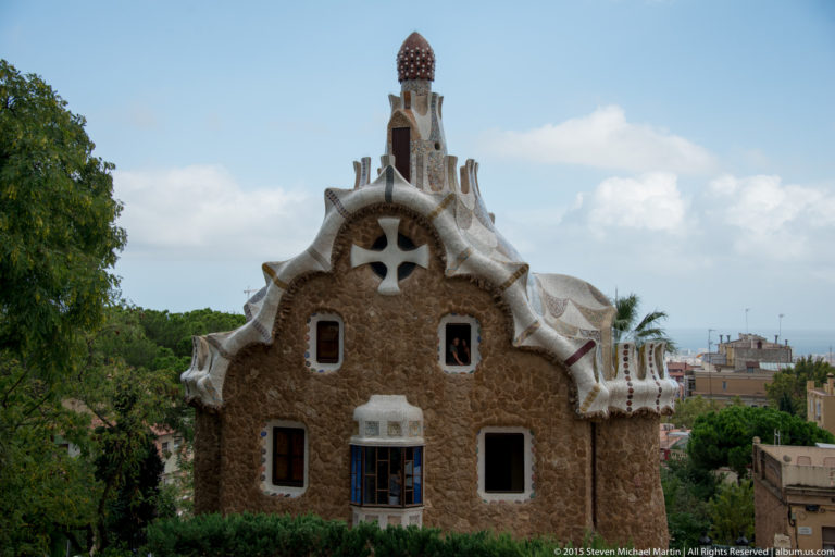 Stone Park Güell entrance house with irregular roofline, small windows, and mosaic chimney.