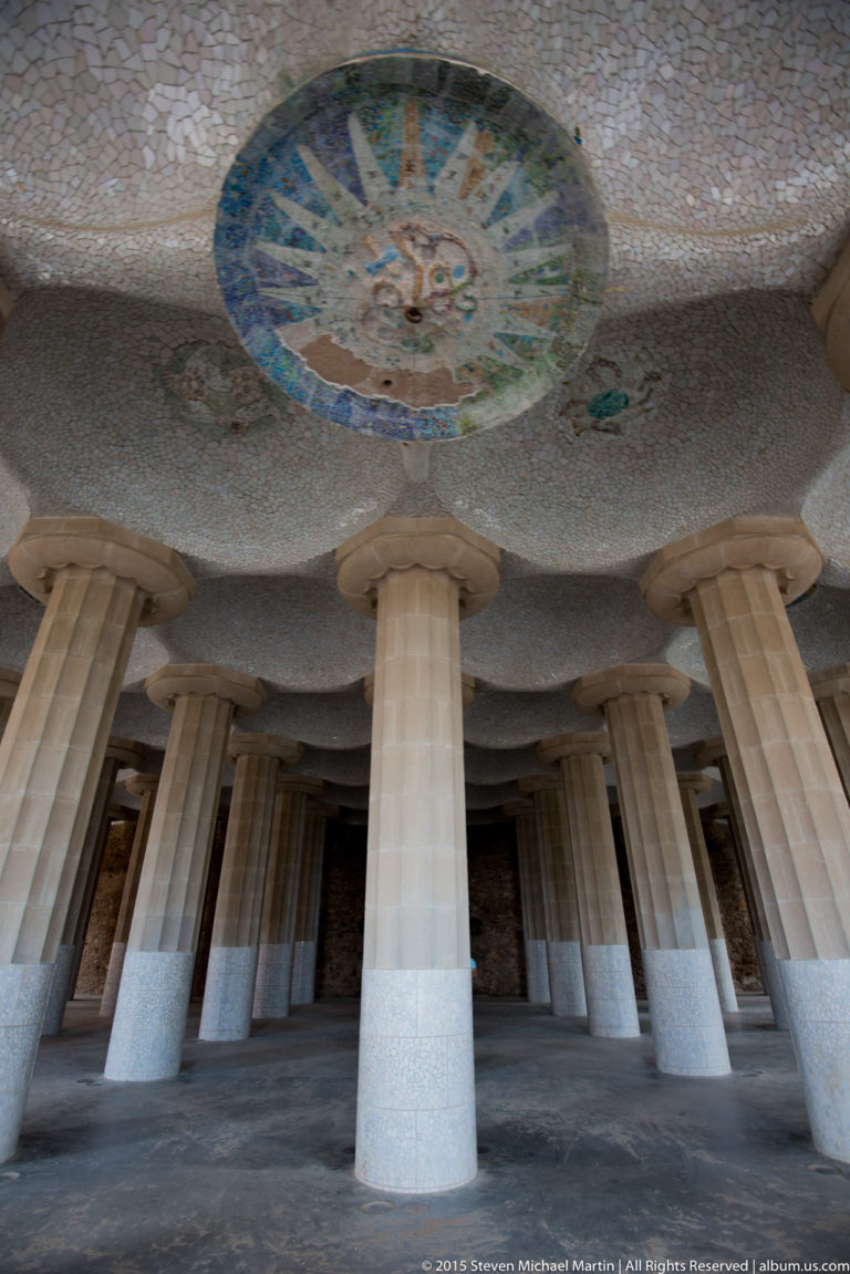 Stone columns support a pale mosaic ceiling with a large circular medallion in Park Güell’s Hypostyle Room.