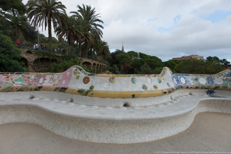 Long undulating white mosaic bench with colorful tile decoration curves across Park Güell’s terrace.