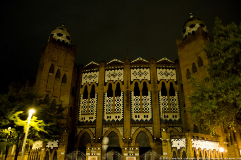 Night view of an ornate brick façade with twin towers and patterned arched windows.