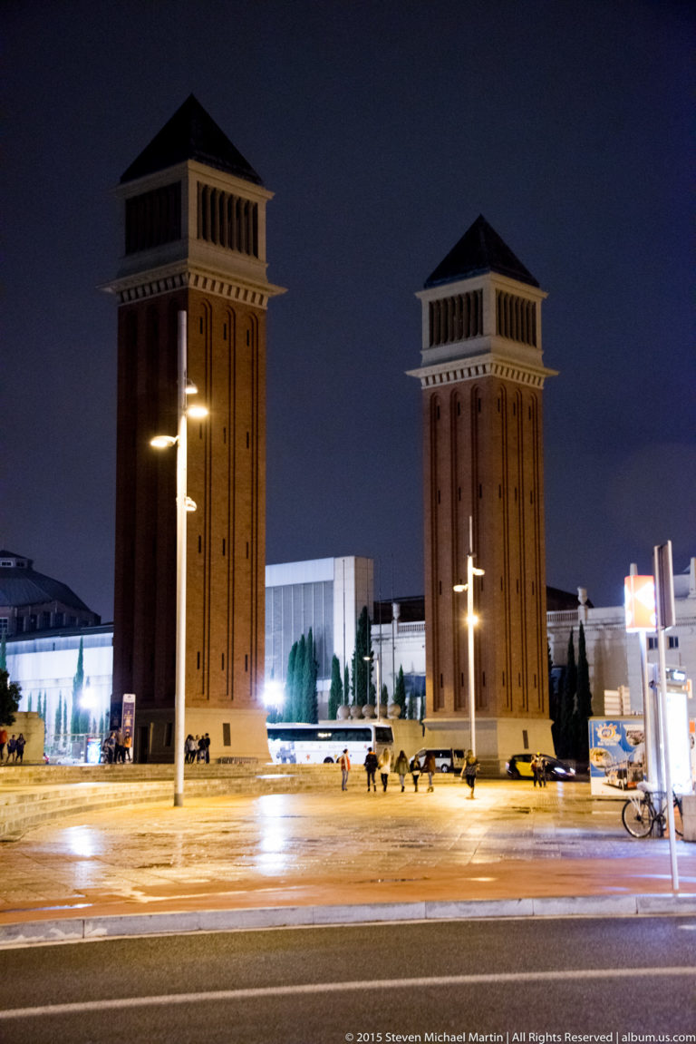 Two tall brick Venetian Towers illuminated at night near Plaça d’Espanya in Barcelona.