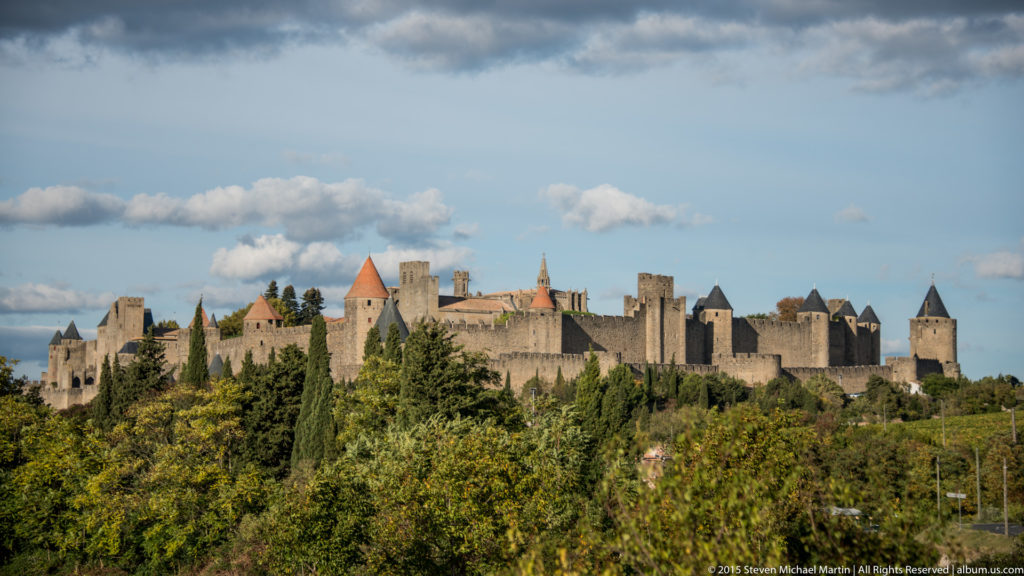 Distant Carcassonne walls and towers extend across the horizon beyond green and autumn-colored trees.