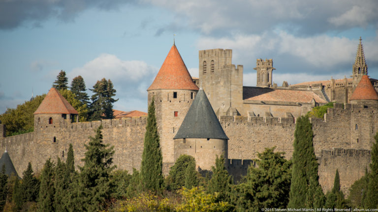 Carcassonne walls and conical-roofed towers stand before the higher roofline and Gothic elements of the basilica inside the city.