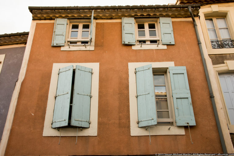Ochre house façade with white-trimmed windows and pale wooden shutters viewed from below in Carcassonne.