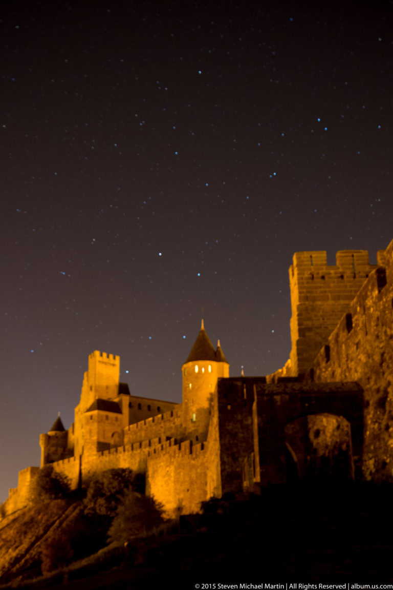 Softly blurred, floodlit walls and towers of Carcassonne beneath a dark sky with visible stars.