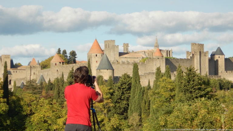 Rear view of a visitor using a tripod camera, with Carcassonne’s towers and crenellated walls filling the background.