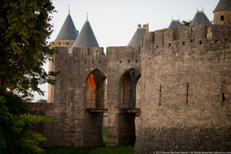 Two tall pointed openings in Carcassonne’s stone fortifications, with roofed towers and crenellated walls behind.