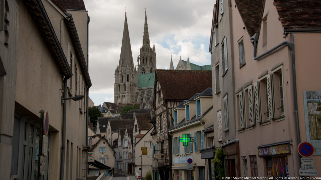 Chartres Cathedral’s two western towers rise above a narrow street lined with houses and shops in the historic center.