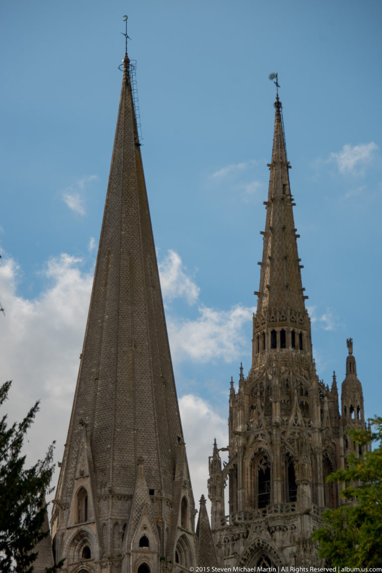 Two contrasting spires of Chartres Cathedral, with a plain pyramidal tower at left and ornate Gothic tower at right.