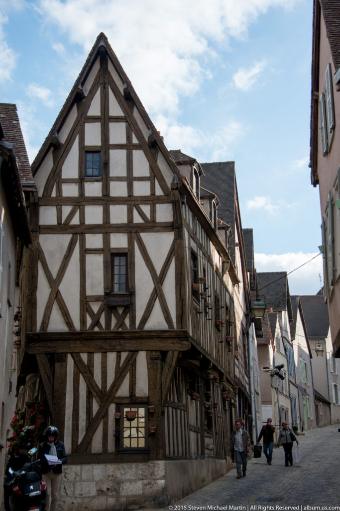 Half-timbered corner house with a projecting upper floor beside a narrow street of historic buildings in Chartres.