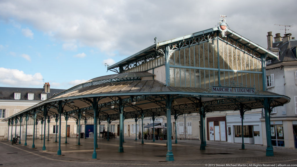 Open iron-and-glass market pavilion marked “Marché aux Légumes” on a paved square in Chartres.