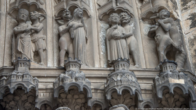 Close view of elongated stone figures beneath carved canopies on a Gothic portal of Chartres Cathedral.
