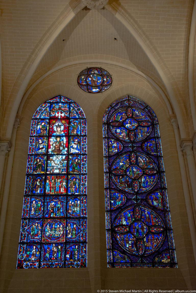 Two stained-glass windows and a small oculus set into pale stone walls inside Chartres Cathedral.