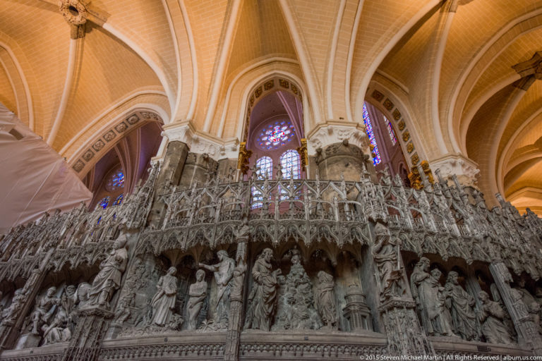 Low-angle view of the richly carved stone choir screen beneath ribbed vaults inside Chartres Cathedral.